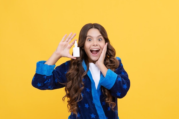 Surprised kid girl in sleepwear using nasal spray against stuffy nose medical