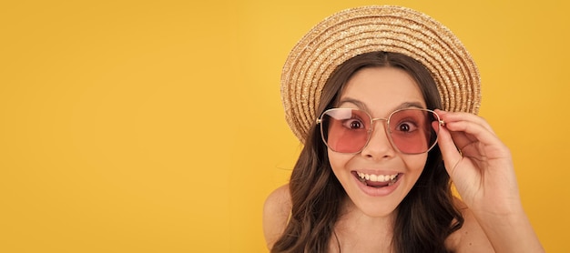 Surprised kid in summer straw hat and glasses has curly hair on yellow background summer sales Child face horizontal poster teenager girl isolated portrait banner with copy space