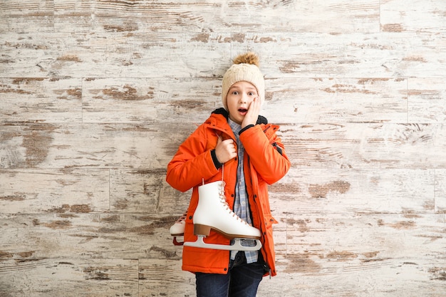 Surprised little boy with ice skates against wooden