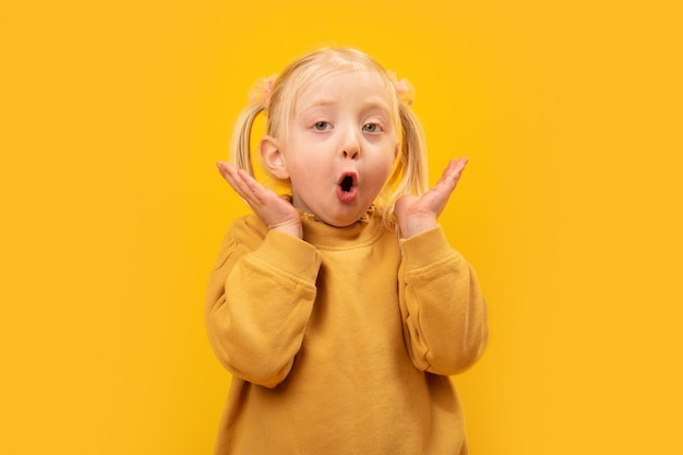 Surprised little girl in yellow clothes on yellow background Blondehaired preschool with wondered face