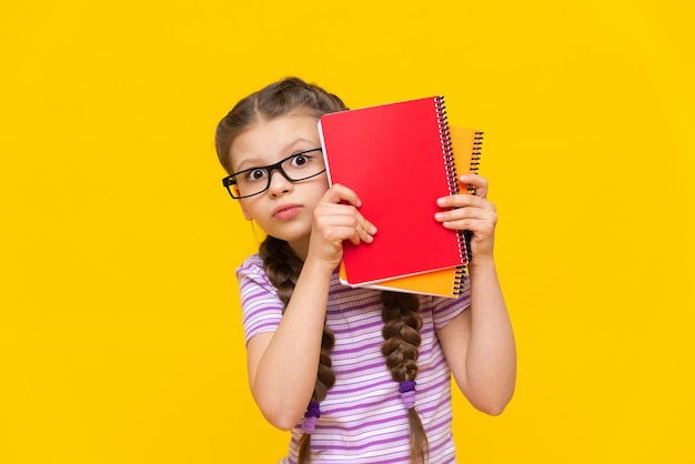 Surprised little schoolgirl on an isolated background A girl with textbooks and notebooks in glasses