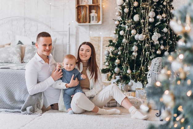 Surprised look. Lovely family sits near the Christmas tree with gift boxes on winter evening