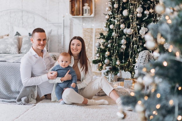 Surprised look. Lovely family sits near the Christmas tree with gift boxes on winter evening