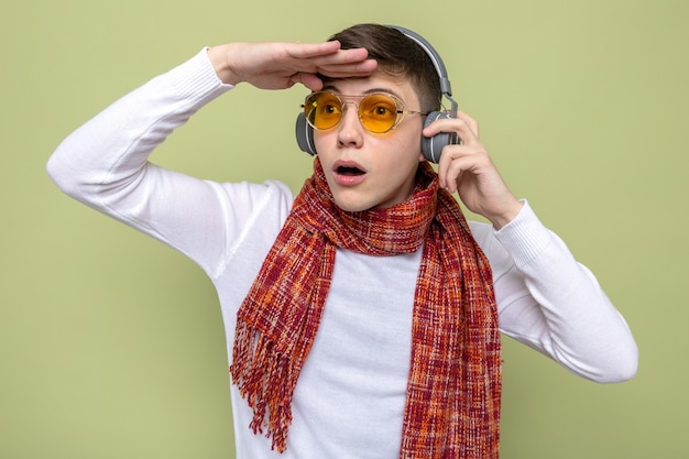 Surprised looking at distance with hand young handsome guy wearing scarf with glasses and headphones 