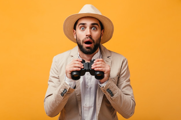 Surprised man in beige outfit posing with binoculars