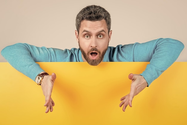 Surprised man behind blank paper banner with copy space for information presenting product