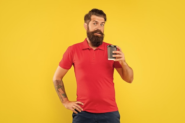 Surprised man in casual red tshirt holding disposable cup with arm akimbo takeaway coffee