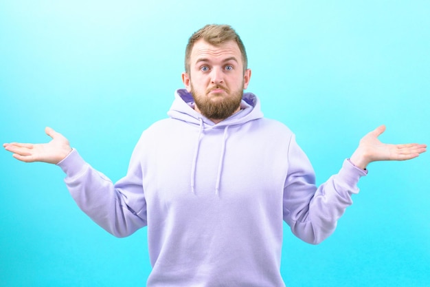 Surprised man in a purple hoodie spreads his hands on a blue background Casual Cheerful Lifestyle Unknowing Doubt Behavior Shock Shoulder Spreading Amazing Trouble Stress Worry Reaction