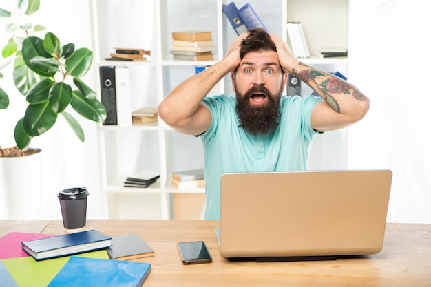 Surprised man with jaw dropped clutching head sitting at laptop in office surprise