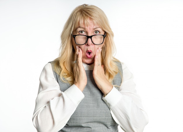 Surprised mature woman in glasses gestures her emotions on a light background.