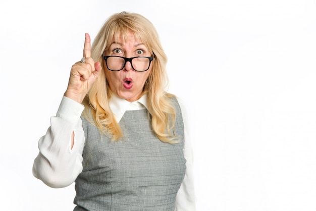 Surprised mature woman with glasses points finger up, isolated on white background.