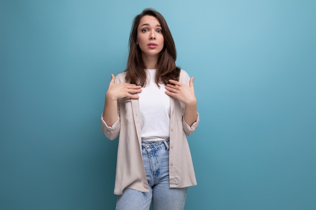 Surprised puzzled s dark haired woman in shirt and jeans on blue background