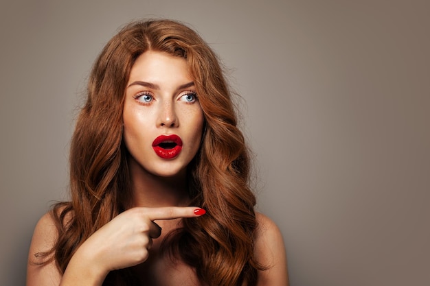 Surprised red head girl pointing finger. Excited redhead model woman pointing on background with empty copy space