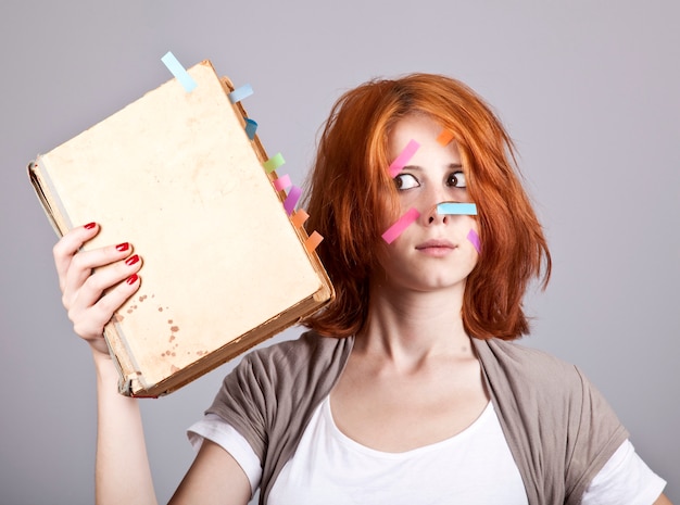 Surprised redhead woman with book and notes on face. 