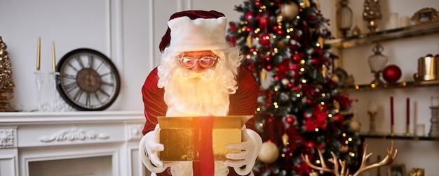 Surprised santa claus with glowing gift near christmas tree new year and merry christmas concept