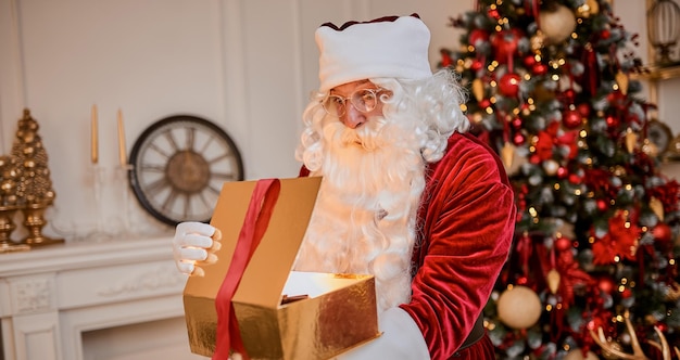 Surprised santa claus with glowing gift near christmas tree new year and merry christmas concept