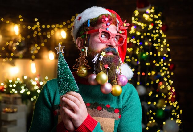 Surprised santa with new year balls in beard holds firtree christmas beard style christmas tree