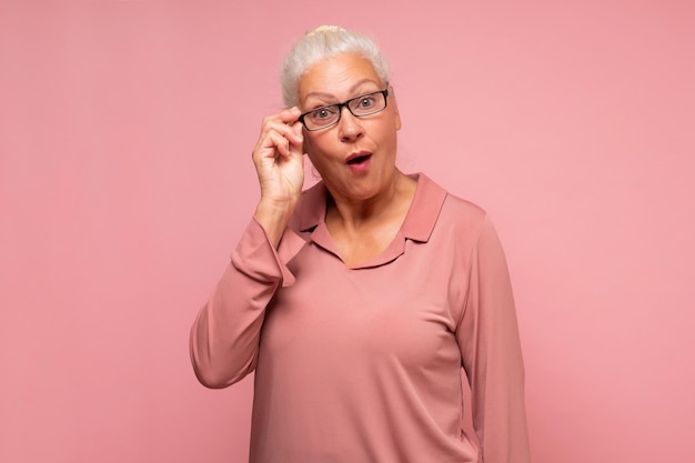 Surprised senior woman looking through glasses otices something unexpected