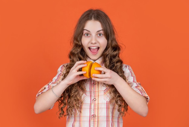 Surprised teen girl hold citric fruit on orange background