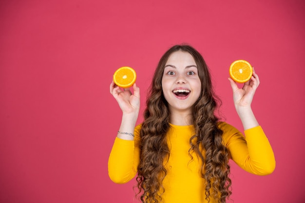 Surprised teen girl hold orange fruit on pink background cpy space