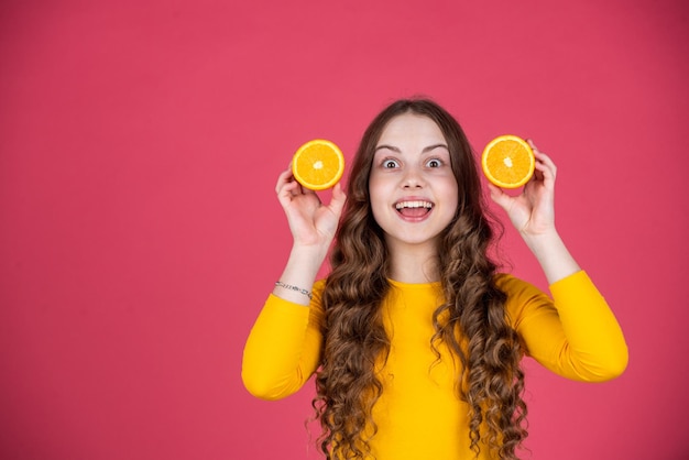 Surprised teen girl hold orange fruit on pink background