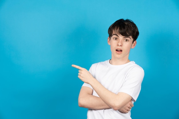 Surprised teenager boy pointing to blue copy space