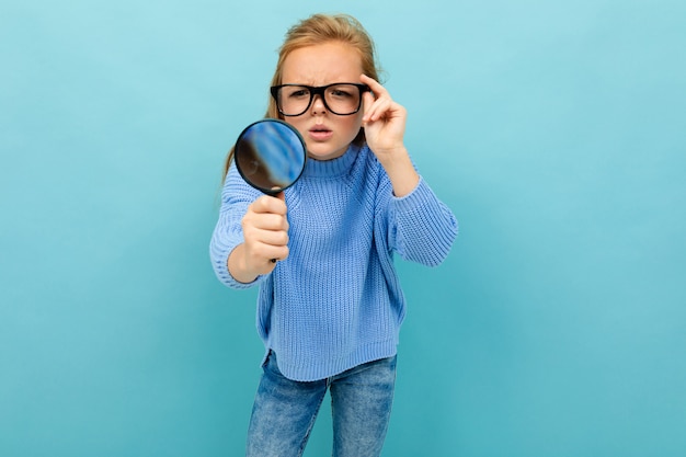 Surprised teenager with a magnifier in glasses on a blue background