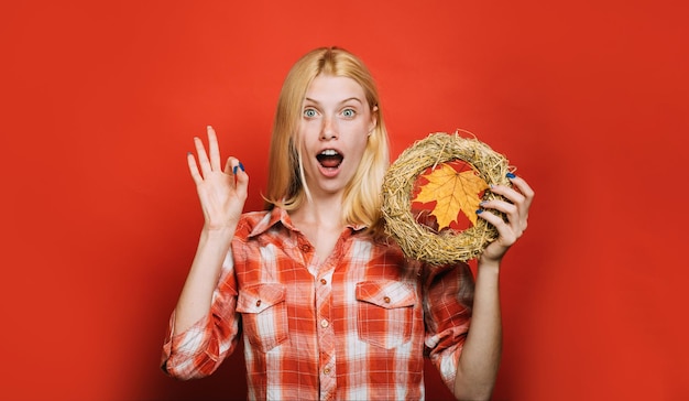 Surprised woman in plaid shirt with decorative autumn wreath showing ok sign handmade decoration