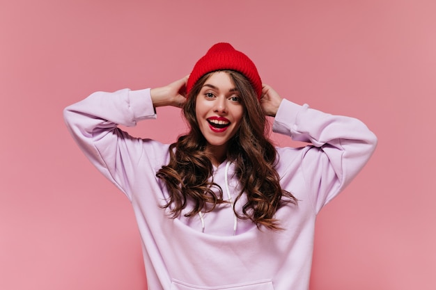 Surprised woman in red hat looks into camera on pink wall