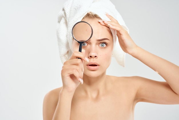 Surprised woman with bare shoulders clean skin magnifying glass in hands health problems