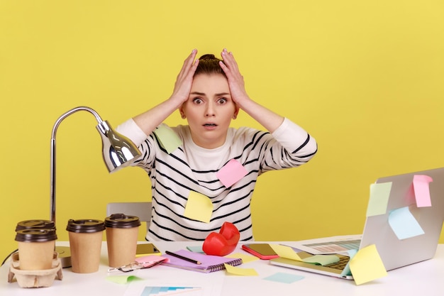 Surprised woman worker covered with sticky notes looking at camera with big eyes and open mouth