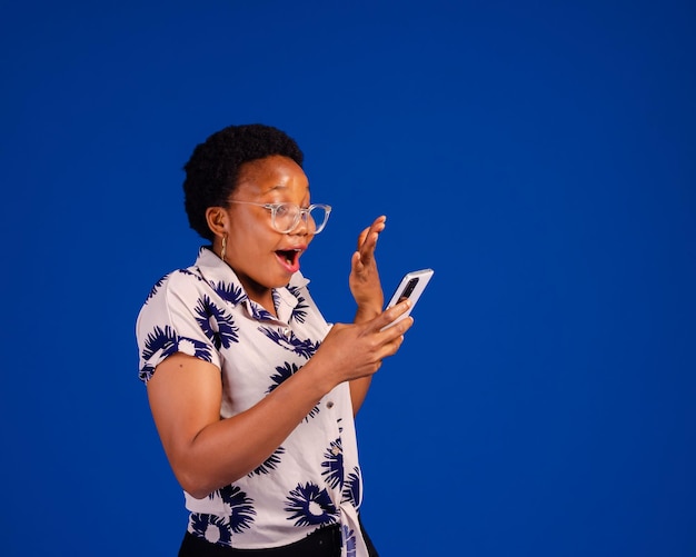 Surprised young African lady using mobile phone with positive expression