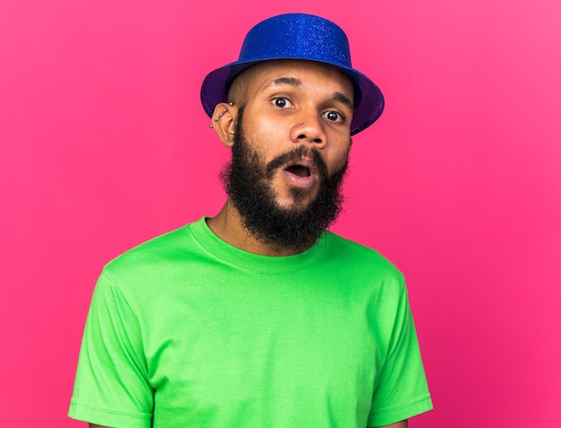 Surprised young afro-american guy wearing party hat isolated on pink wall