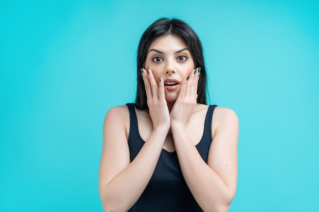 Surprised young brunette woman isolated on turquoise background