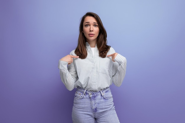 Surprised young brunette woman in shirt on studio background