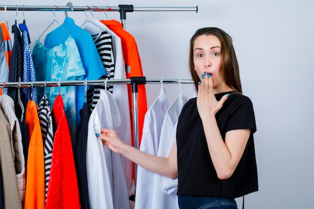 Surprised young girl is holding hand on mouth on clothes background