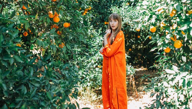 Surprised young girl in orange dress is posing to camera in orange garden