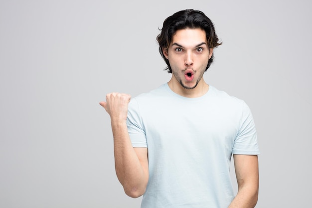 surprised young handsome man looking at camera pointing to side isolated on white background with copy space