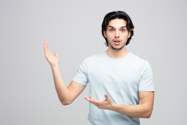 surprised young handsome man looking at camera showing empty hands isolated on white background