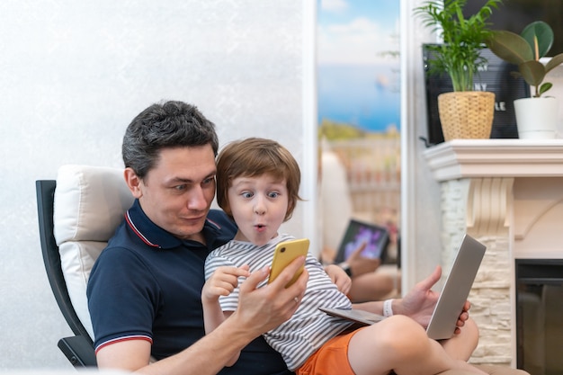 Surprised young man sit on computer using laptop relax with preschooler son