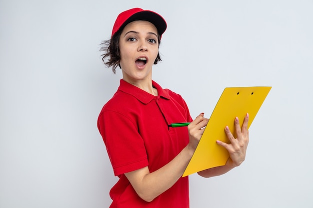 Surprised young pretty delivery woman holding clipboard