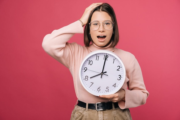 Surprised young woman is holding hand on head and a white round clock