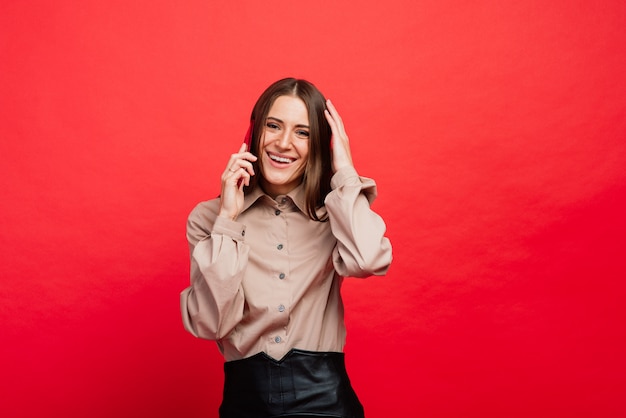 Surprised young woman using smartphone on red background