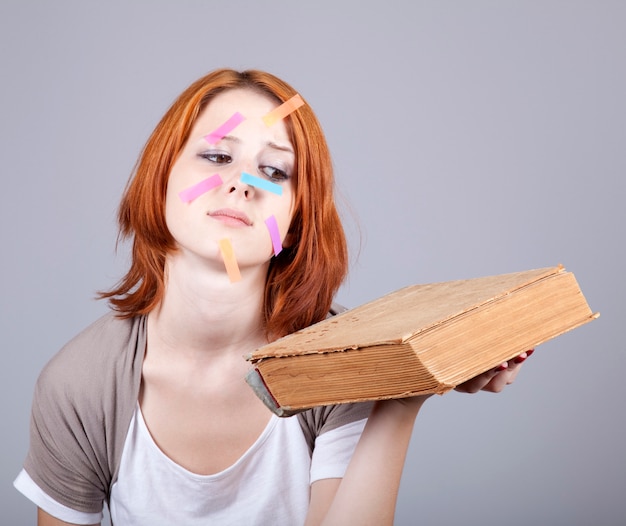 Surprised young woman with book and  notes on face. Portrait on grey background