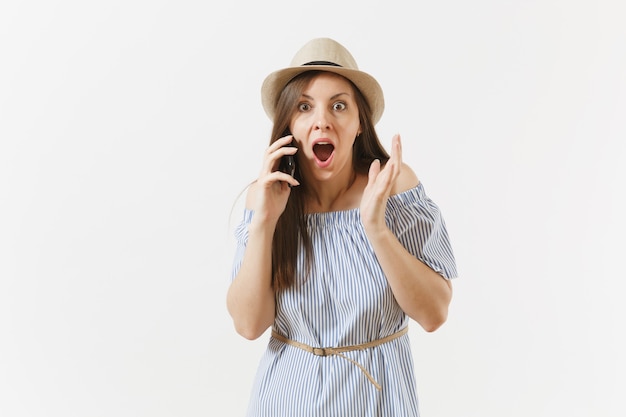 Surrprised upset young woman dressed blue dress, hat has some problems, hears fake news or unexpected rumor in mobile phone isolated on white background. People, sincere emotions, lifestyle concept.