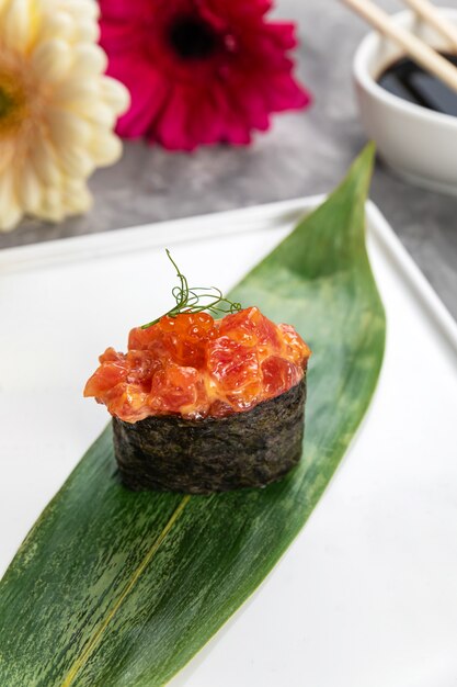 Sushi on a banana leaf with sauce on a white plate