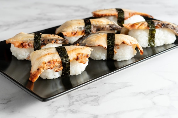 Sushi nigiris with eel fish rolled with a strip of seaweed served on a black plate on a marble table