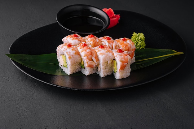 Sushi roll covered with shrimp meat on black ceramic plate