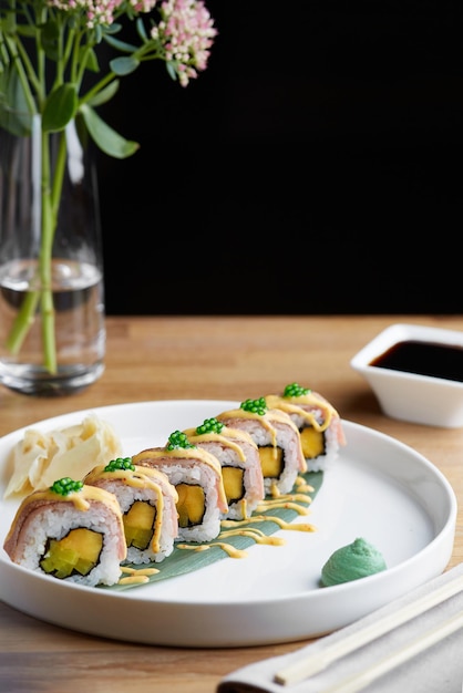 Sushi roll with bacon on wooden plate with flowers and soy sauce close up. restaurant table concept