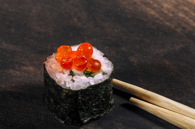 Sushi roll with red caviar on the dark wooden background , eating sushi roll in restaurant, selective focus. Close up.